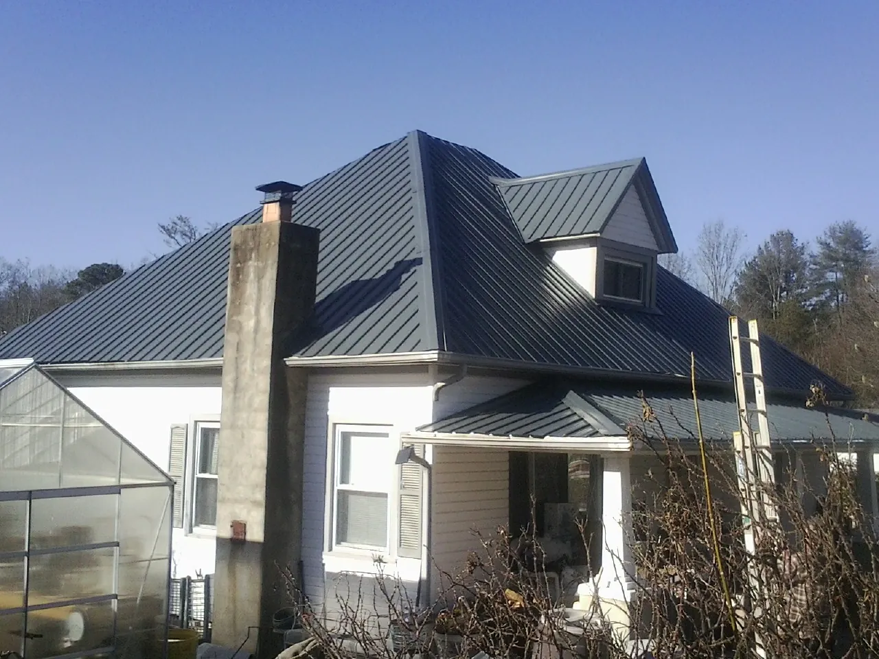 Dark blue standing seam metal roof on a white farmhouse with dormer — Slate & Tile Roof Repair by Roofing Brothers in Cosby