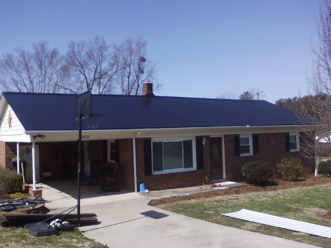 Finished dark blue metal roof on a brick ranch with a carport in Cosby