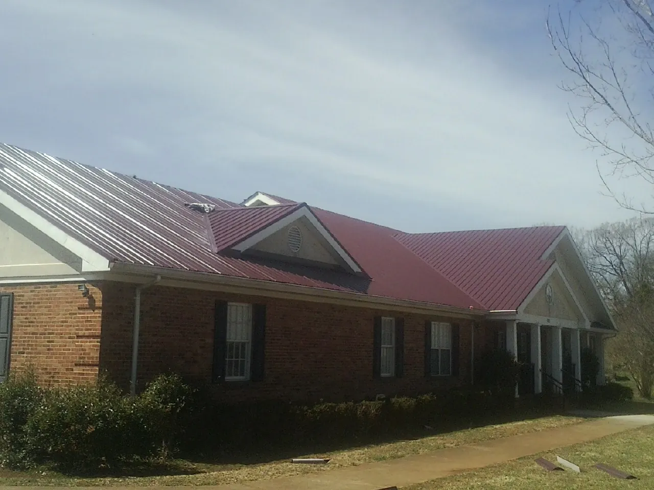 Red metal roof with gabled entries on a long brick building, from a Hail Damage Roof Repair job in Cosby