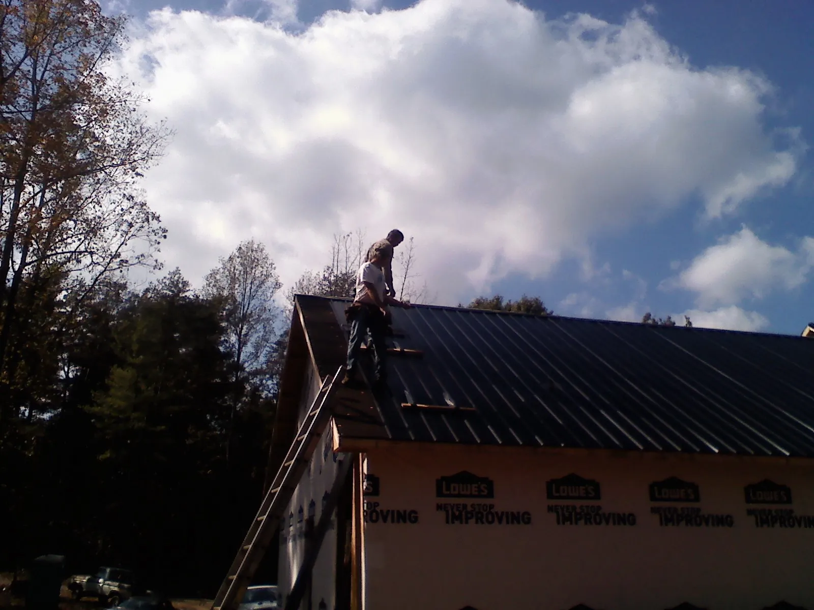 Roofer fastening dark metal panels high against a cloudy sky, from a Roof Inspection job in Cosby
