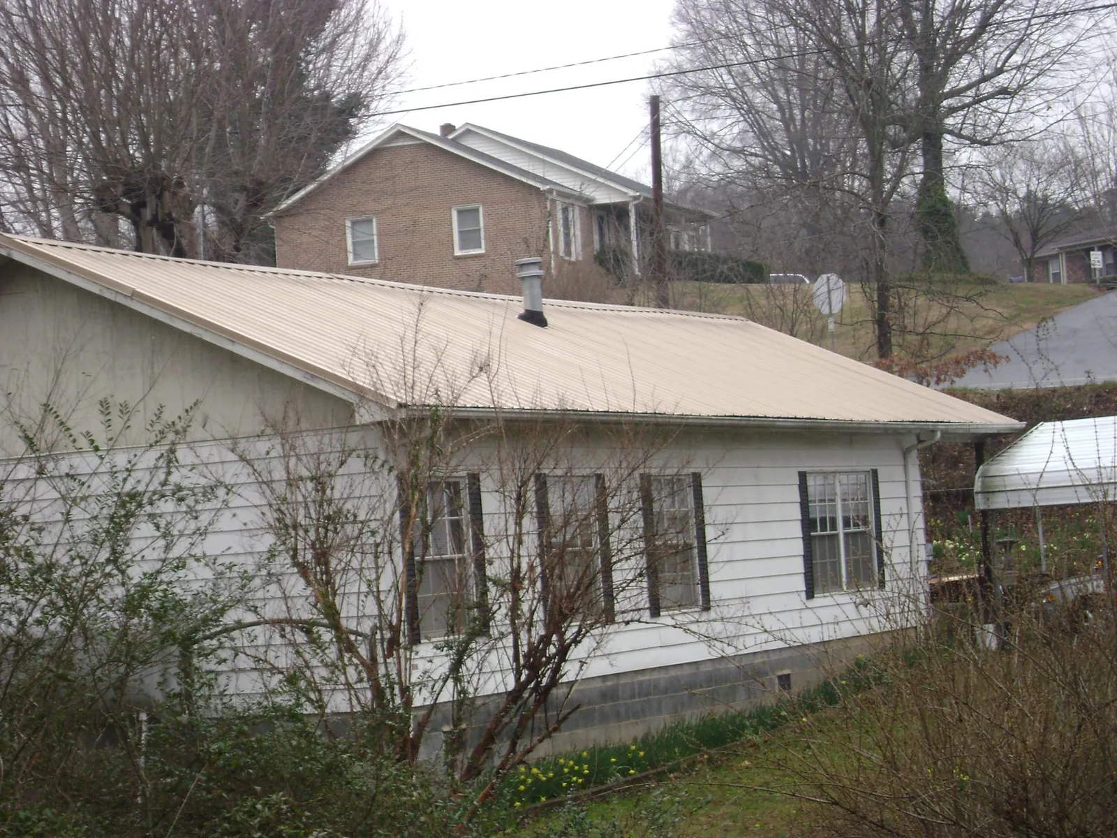 Tan metal roof on a white sided house set into a hillside — Commercial Roofing by Roofing Brothers in Cosby