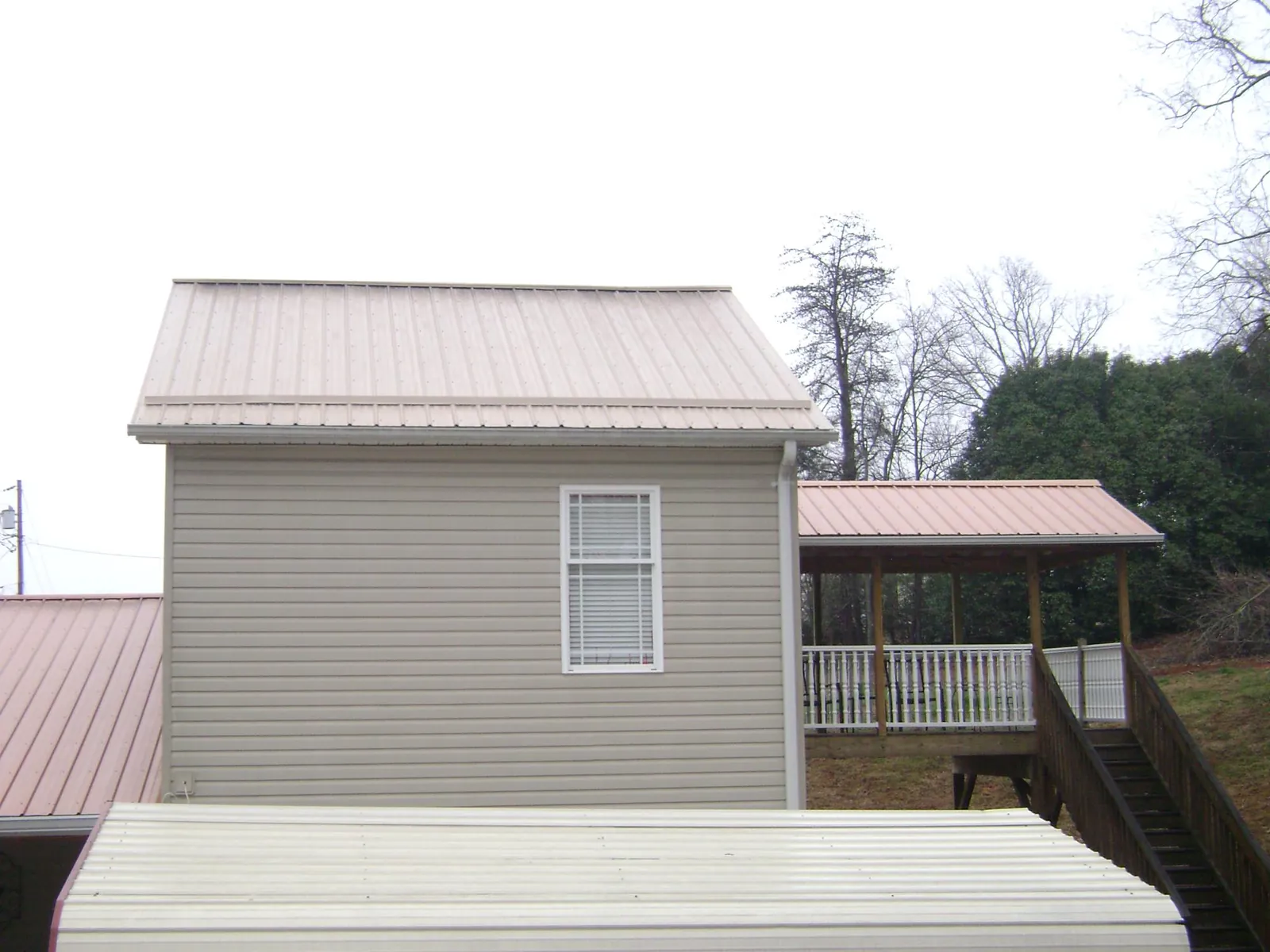 Tan metal roofs on a two story addition and attached porch, from a Roof Replacement job in Cosby